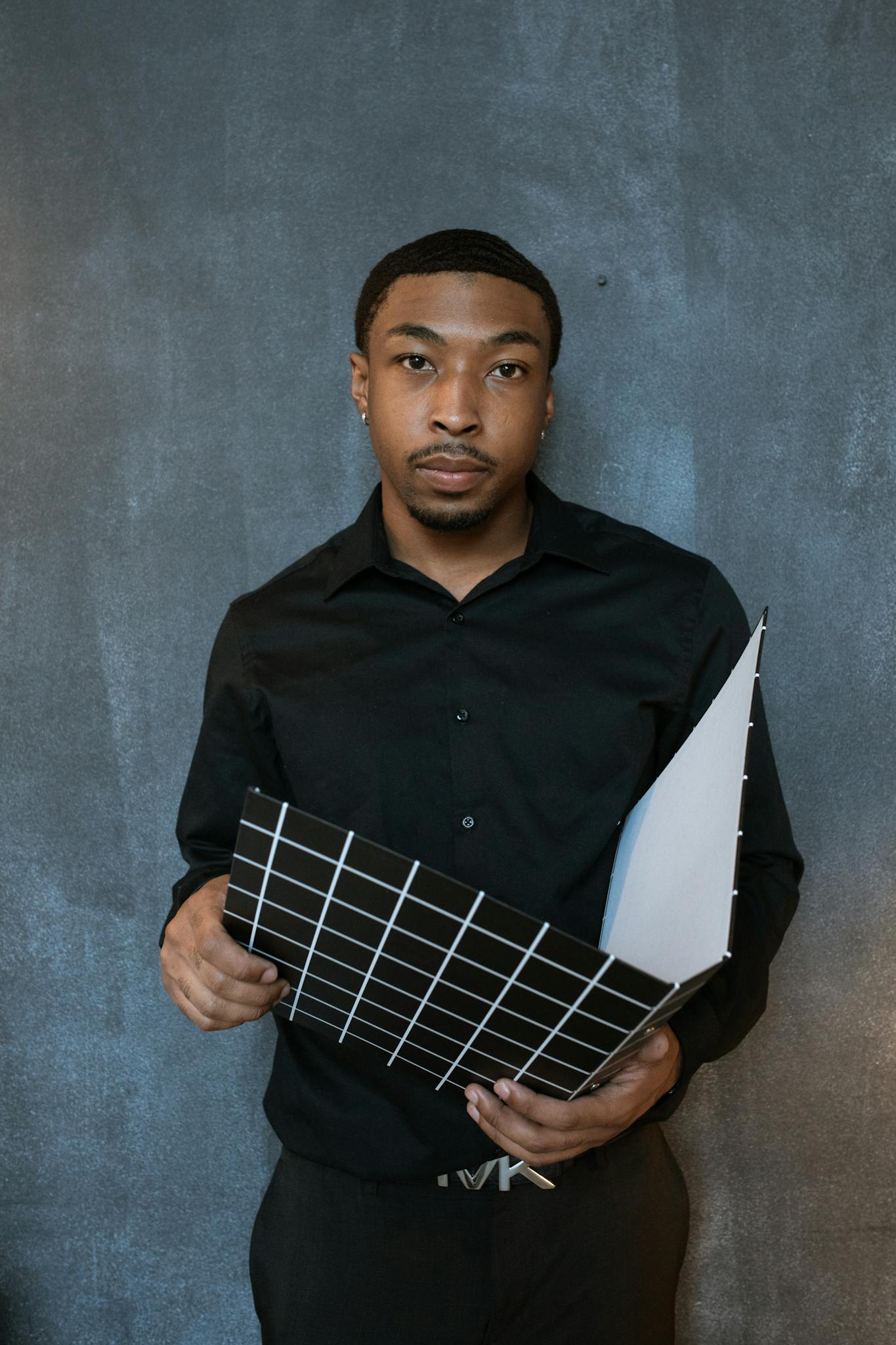 Portrait of a focused Black businessman in a black shirt holding a grid file against a textured wall.